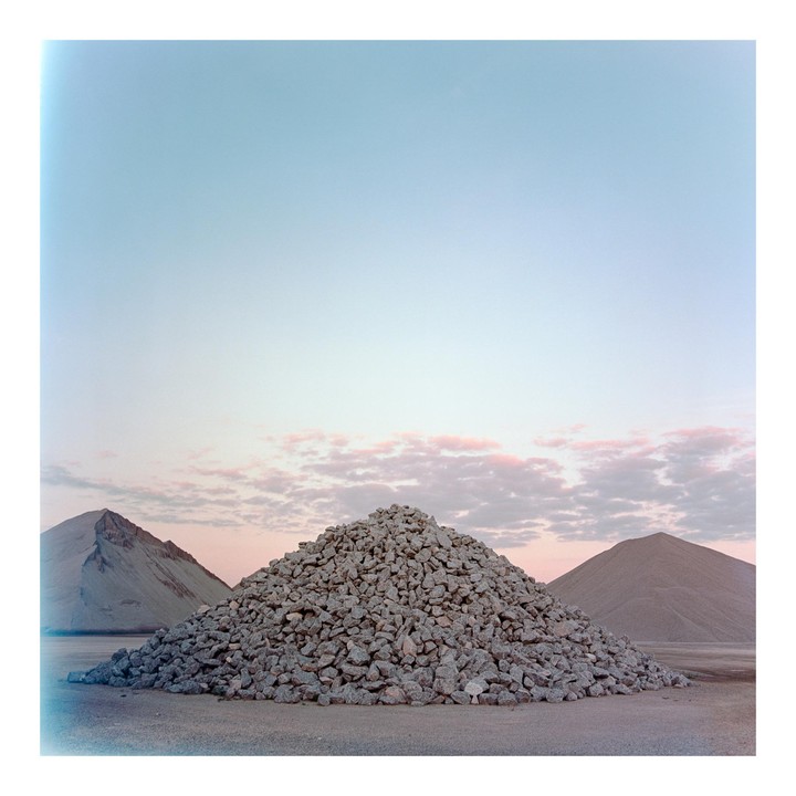 A large mound of gravel sits in the foreground with two smaller mounds behind it under a sky with pink clouds.