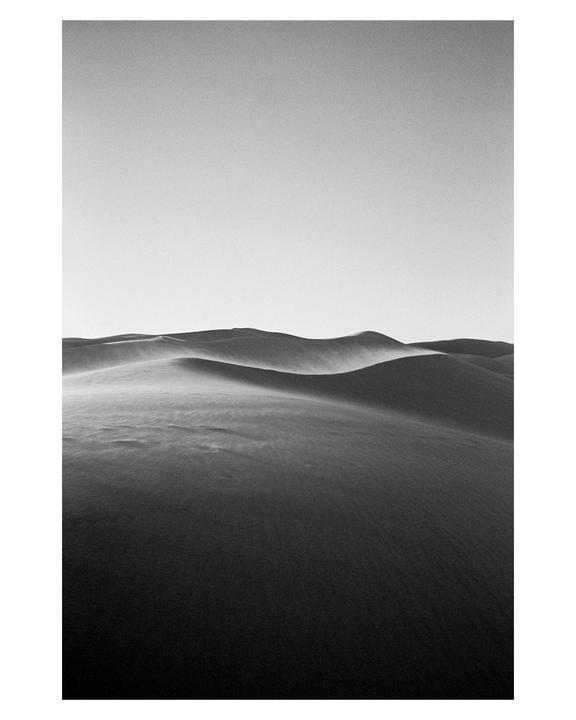 A black and white landscape shows sand dunes with a clear sky above.