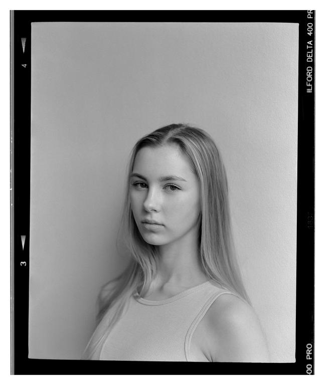 A young woman with long hair looks directly forward in a portrait.