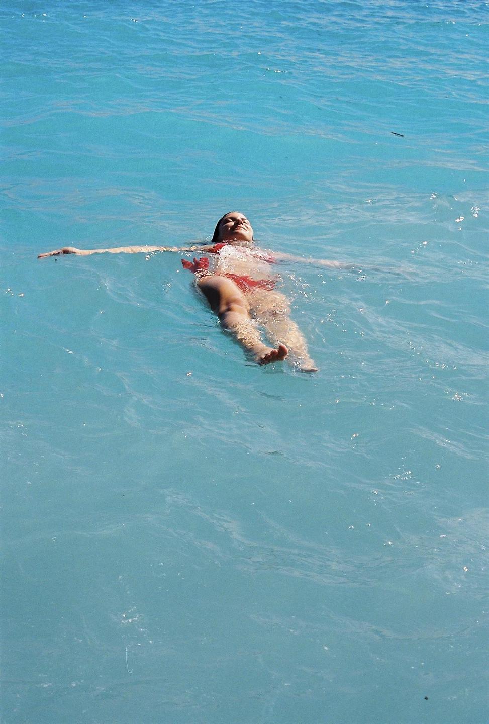 A woman in a red swimsuit floats on her back in blue water.