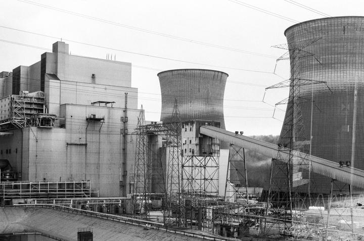A large industrial complex with multiple cooling towers and power lines is shown under a bright sky.
