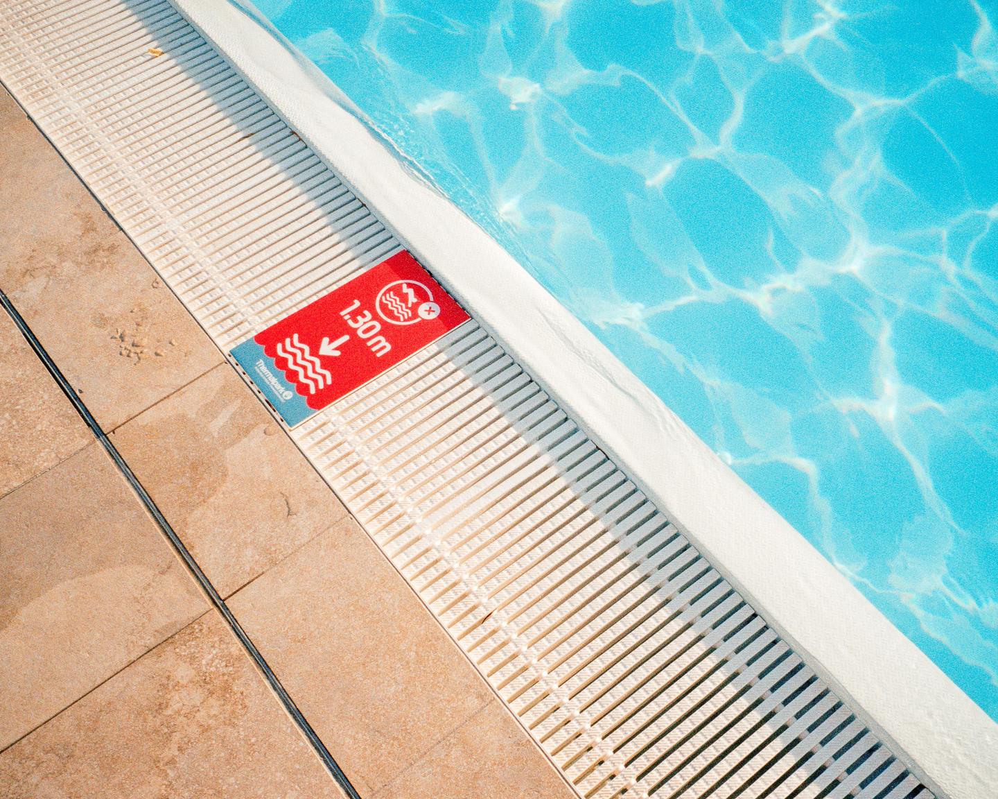 A red sign indicating a depth of 1.30 meters is visible at the edge of a swimming pool with blue water.