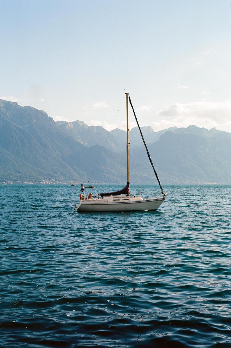 A sailboat floats on a lake with mountains in the background.