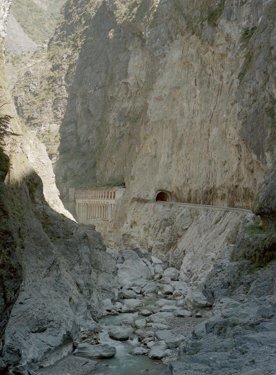 A river flows through a rocky gorge with a road and tunnel built into the cliff face.