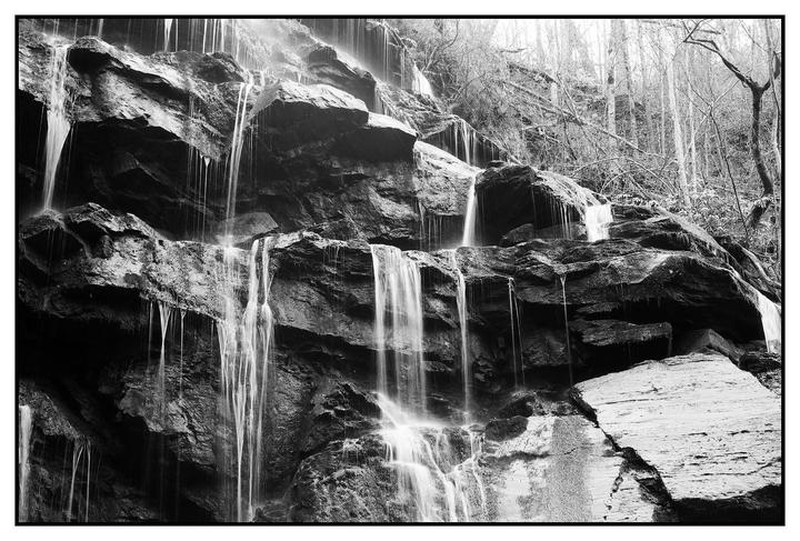 Water cascades down a rocky cliff face with bare trees visible at the top.