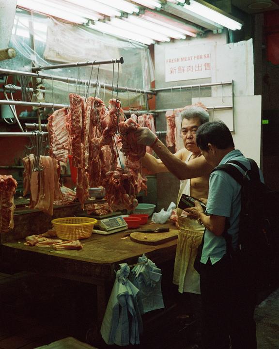 A man sells meat to a customer in a market stall in Hong Kong.