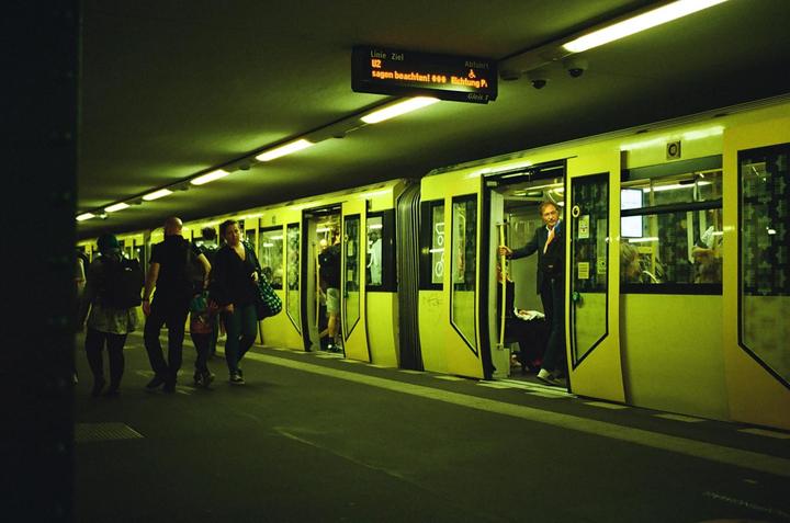People walk along a subway platform as a man stands in the open door of a subway car.
