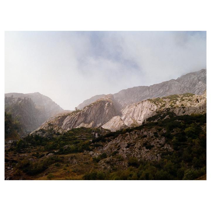 Sunlight illuminates the rocky slopes of a mountain range partially obscured by mist.