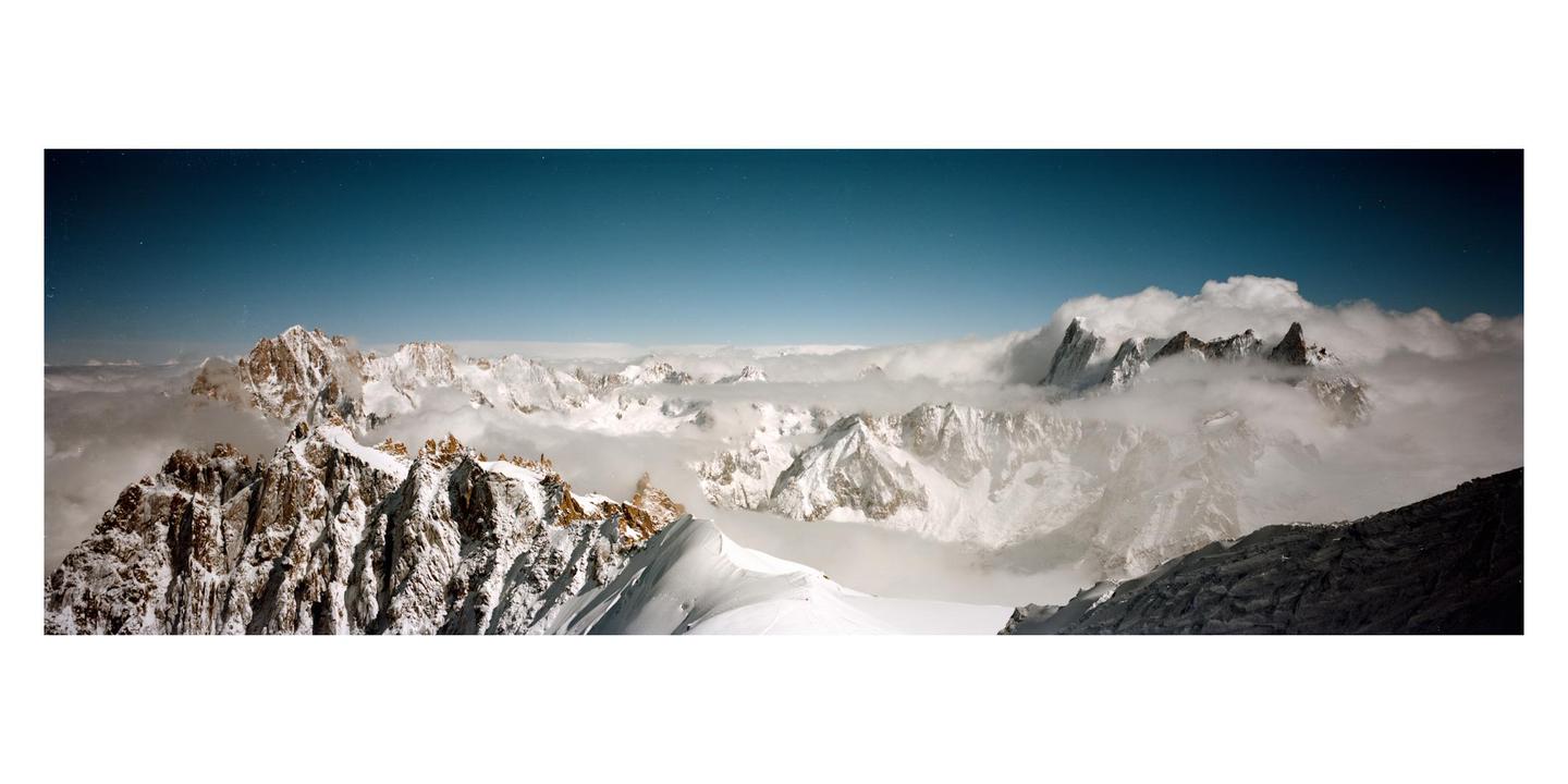 Snow-covered mountain peaks are visible through a layer of clouds under a clear blue sky.