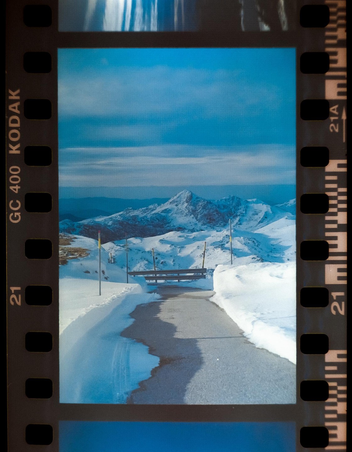 A snowy mountain landscape is seen through a film rebate with a road leading towards the mountains.