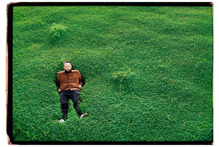 A man is lying on his back in a field of green clover.