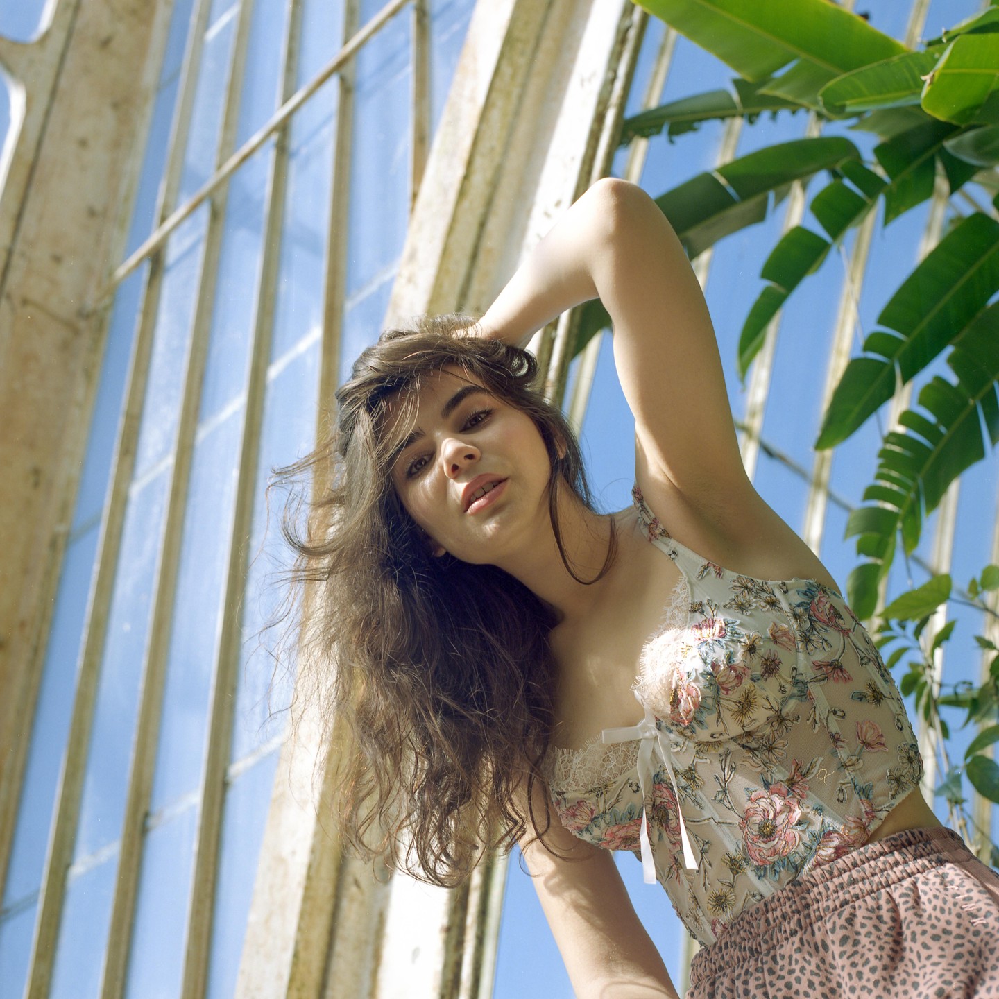 A woman with long hair poses for a portrait in a greenhouse.