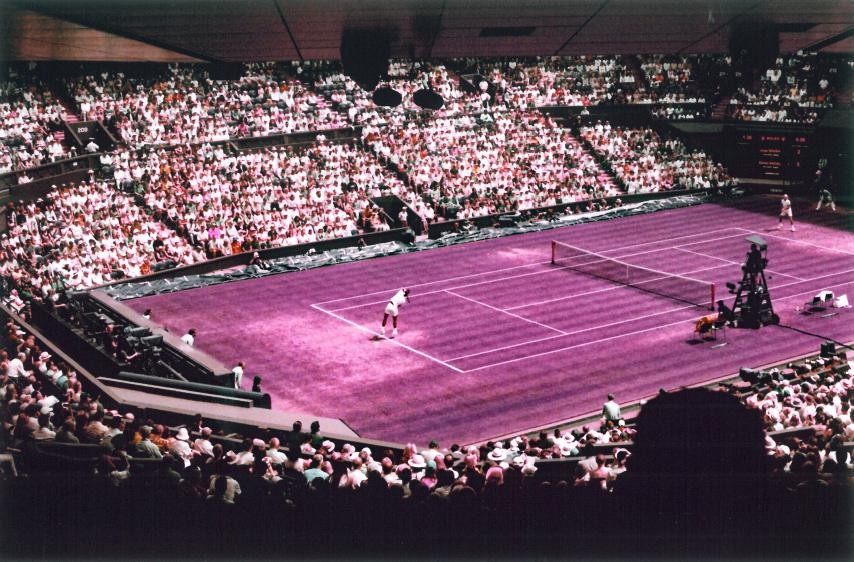 A tennis player serves on a purple court surrounded by a large crowd in a stadium.