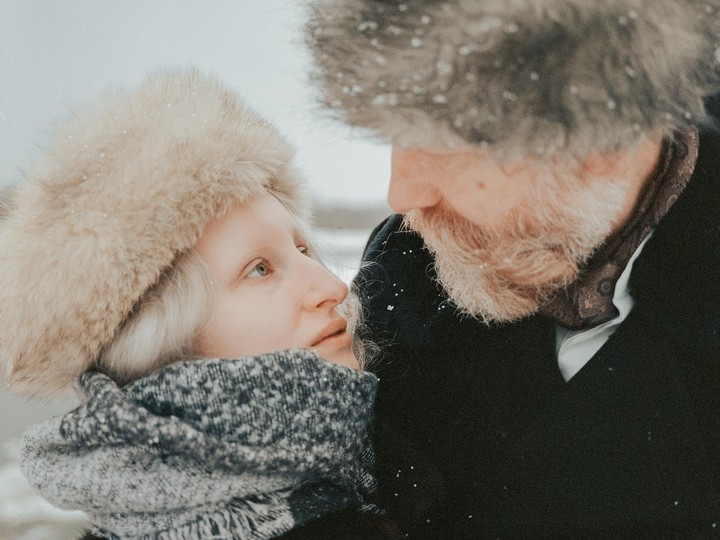 A woman in a fur hat and a man with a beard look at each other in the snow.