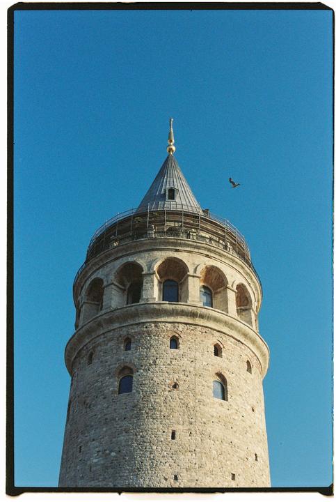 A stone tower with a conical roof and a bird flying in the clear blue sky.