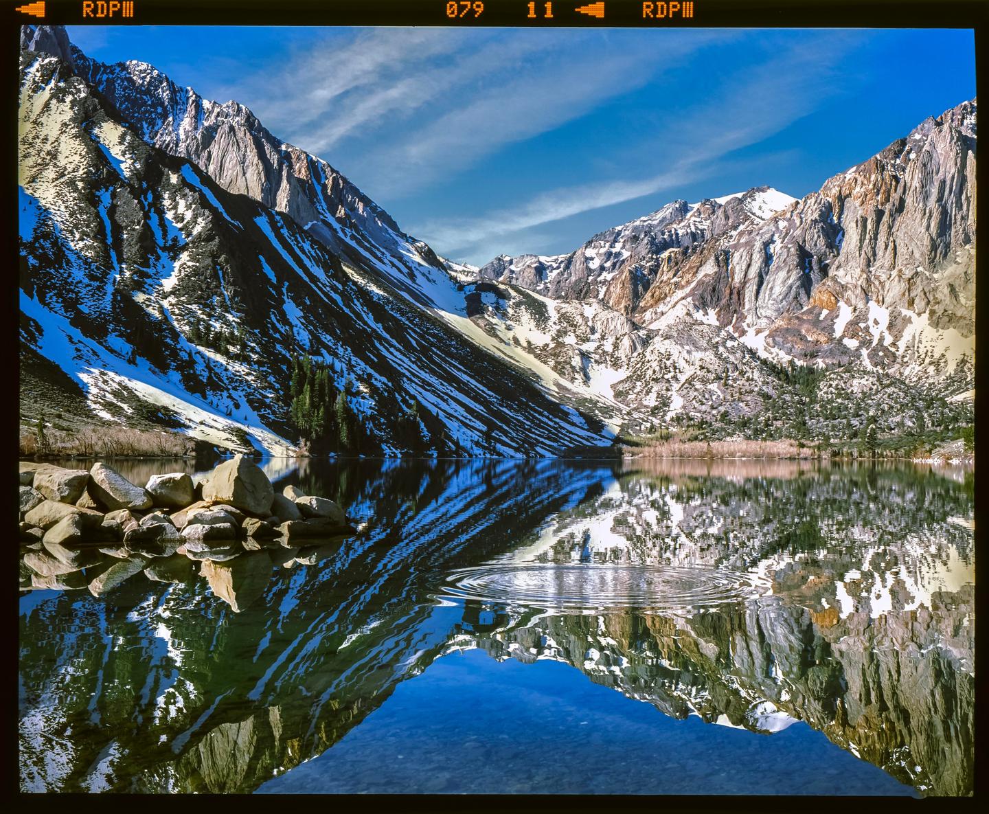 A mountain range with snow is reflected in a lake with ripples in the water.