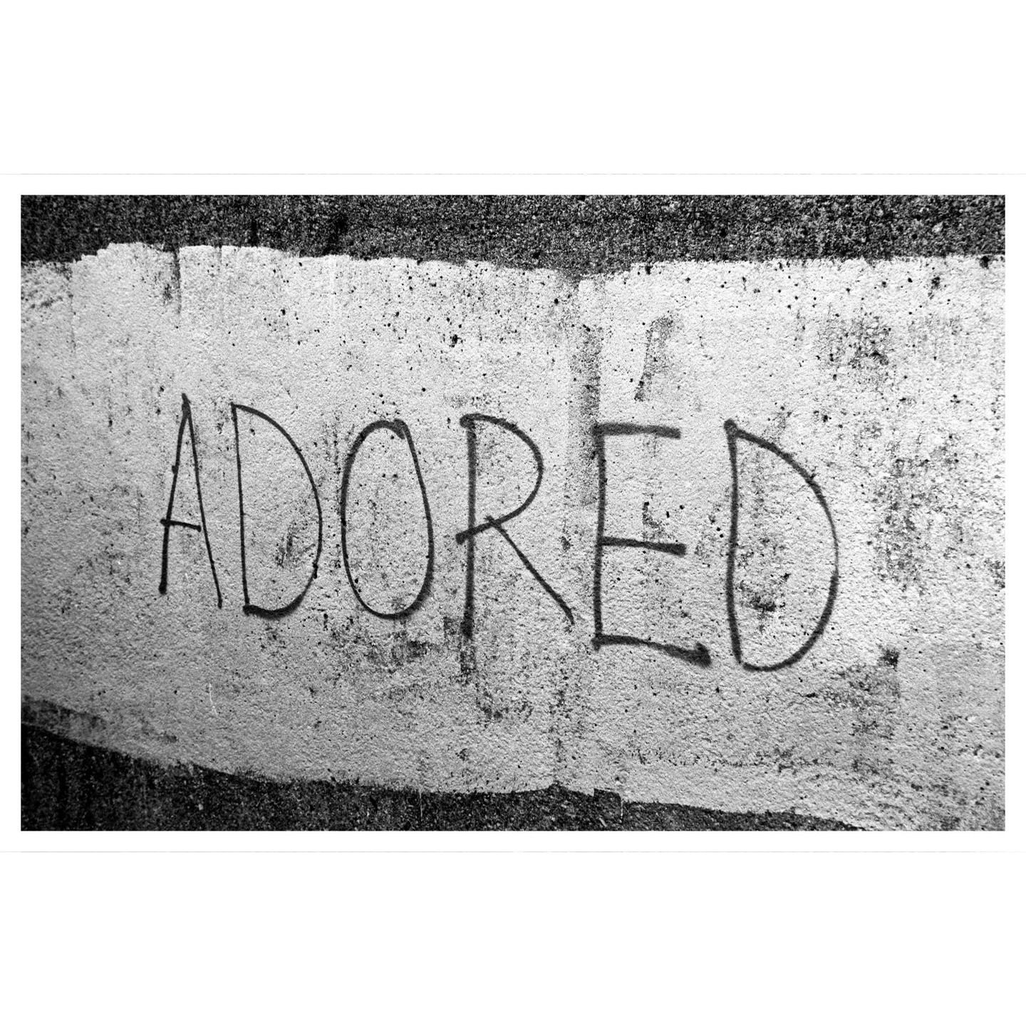 The word "ADORED" is written in black on a white painted concrete surface.