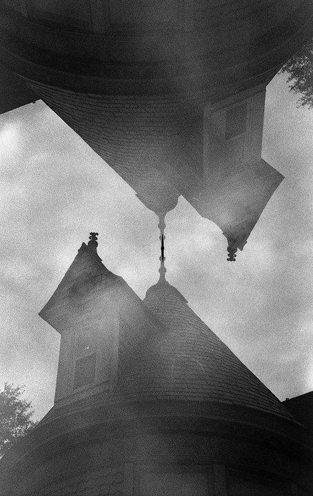 A double exposure shows two inverted images of a building's turret and roofline against a cloudy sky.