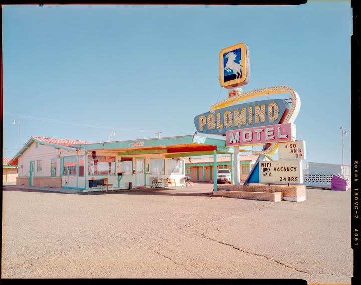 A motel with a large neon sign stands under a clear sky.