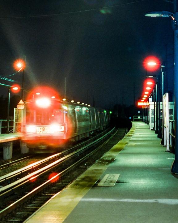 A train with bright headlights approaches a station platform at night.