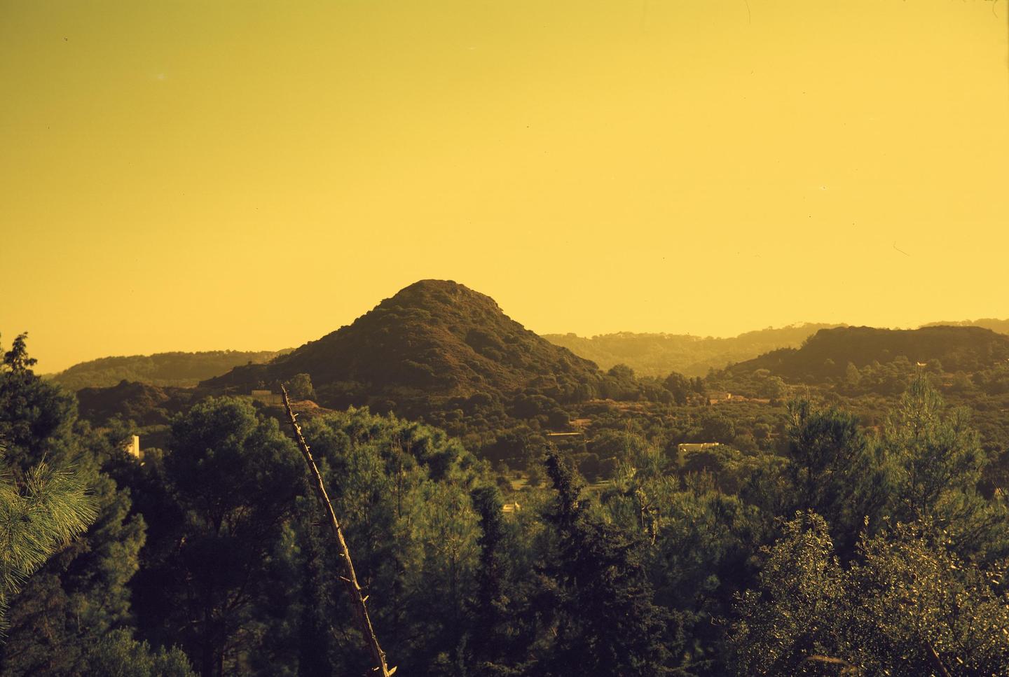 A yellow-tinted landscape shows a mountain and hills covered in trees under a bright sky.