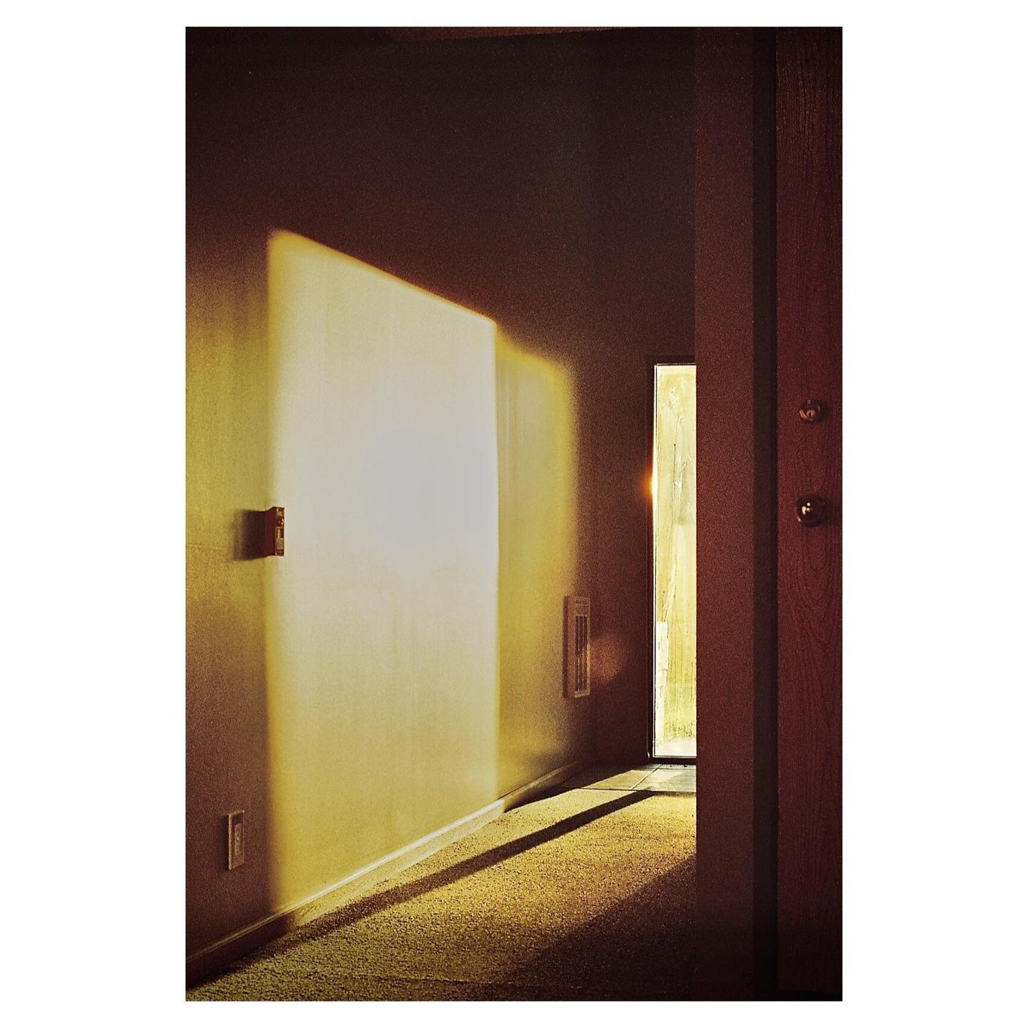 Sunlight streams into a hallway with a closed door on the right.