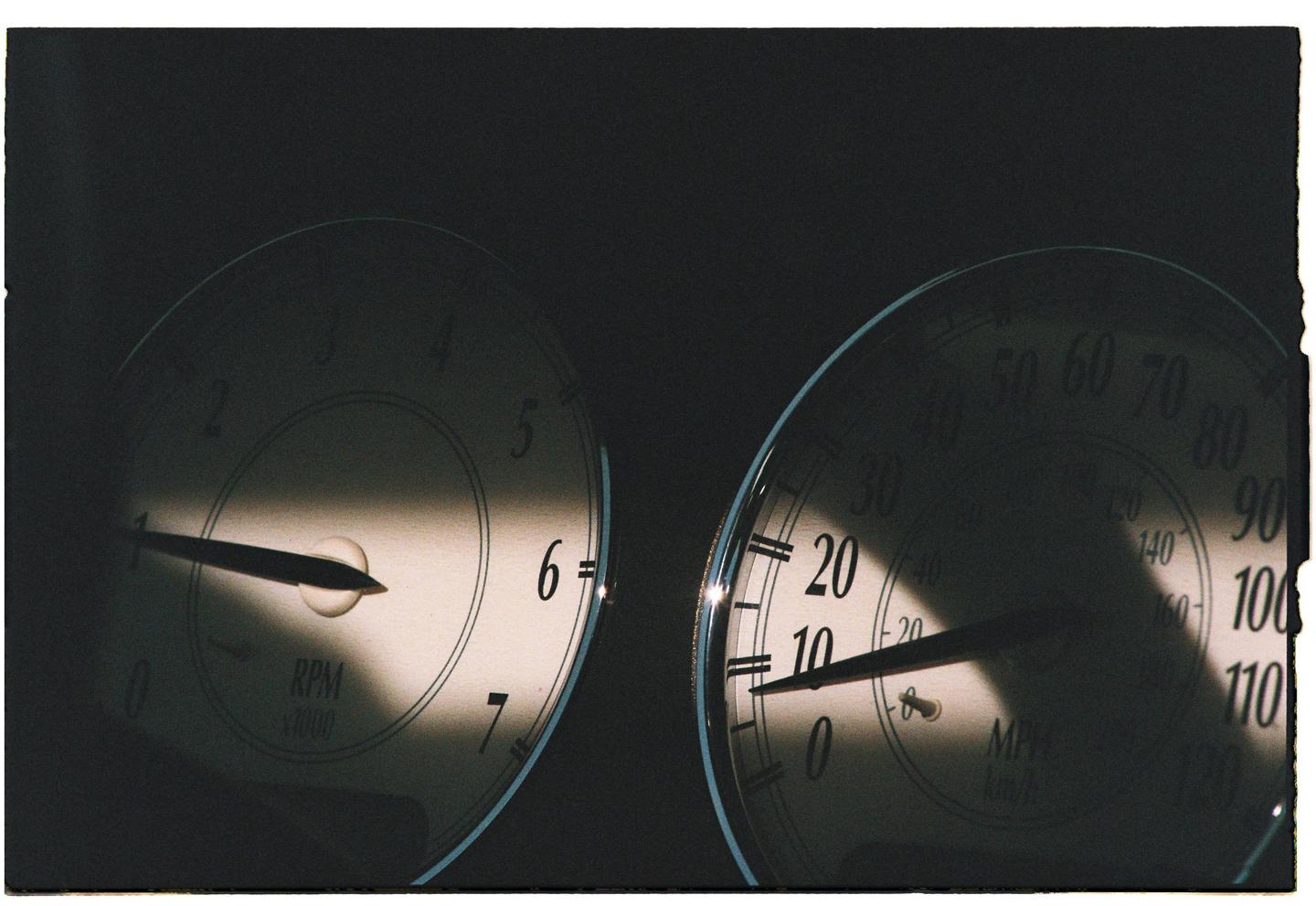 Two vehicle gauges are partially illuminated by a diagonal beam of light.