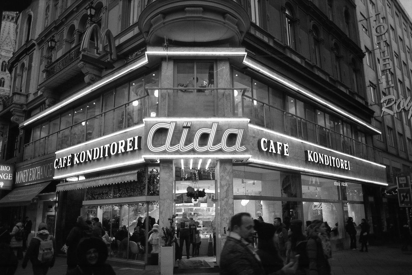 A cafe and pastry shop with neon signs is visible on a city street at night.