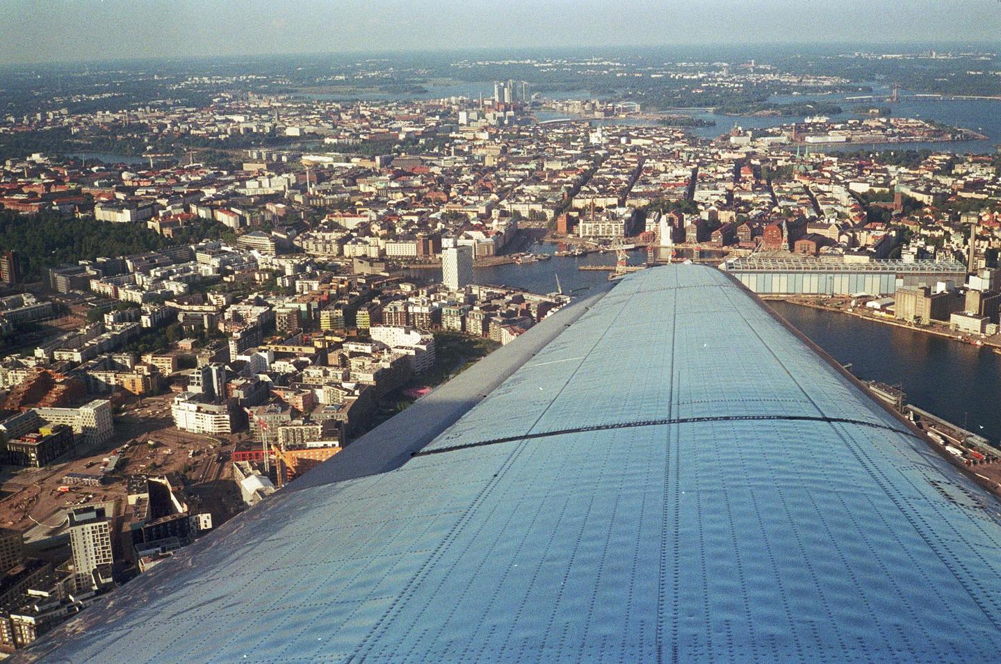 An aerial view shows a city with a large body of water and a plane wing in the foreground.