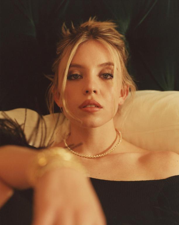 A woman with blonde hair and a gold necklace is looking directly at the viewer.