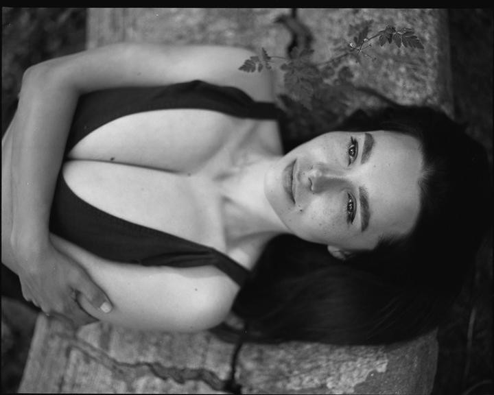 A woman with long dark hair and freckles lies on her back, looking up at the viewer.