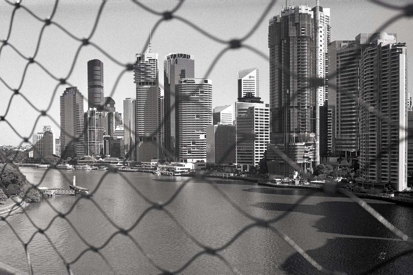 A city skyline with tall buildings is visible across a body of water, viewed through a fence.