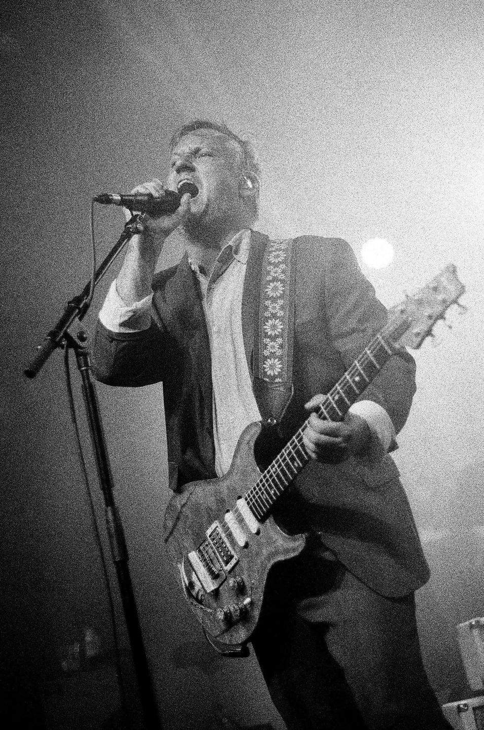 A man sings into a microphone while playing an electric guitar on stage.