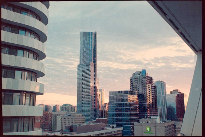 A cityscape with tall buildings is visible under a cloudy sky during sunset.