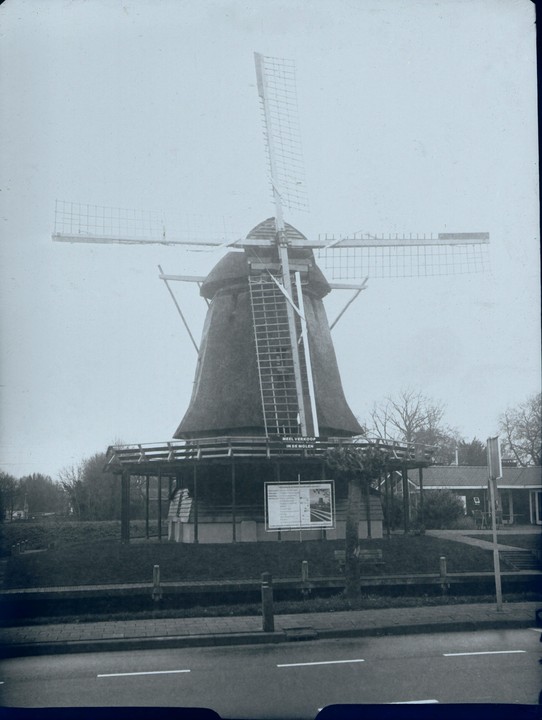 A large windmill with a thatched roof stands next to a road.