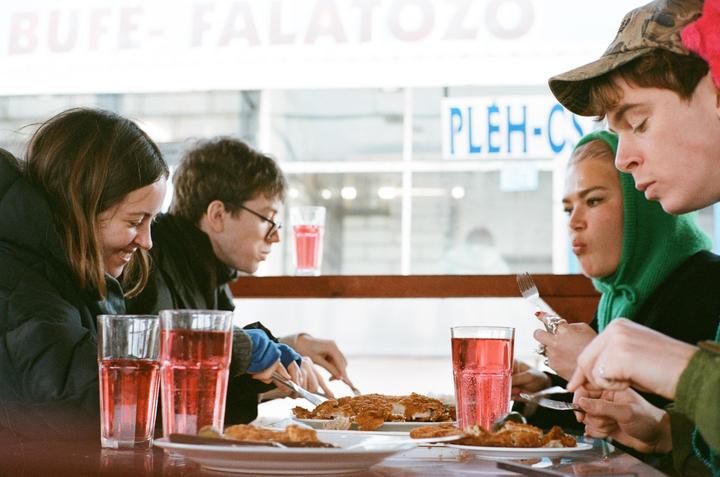 Four people are seated at a table, eating and drinking pink beverages from tall glasses.