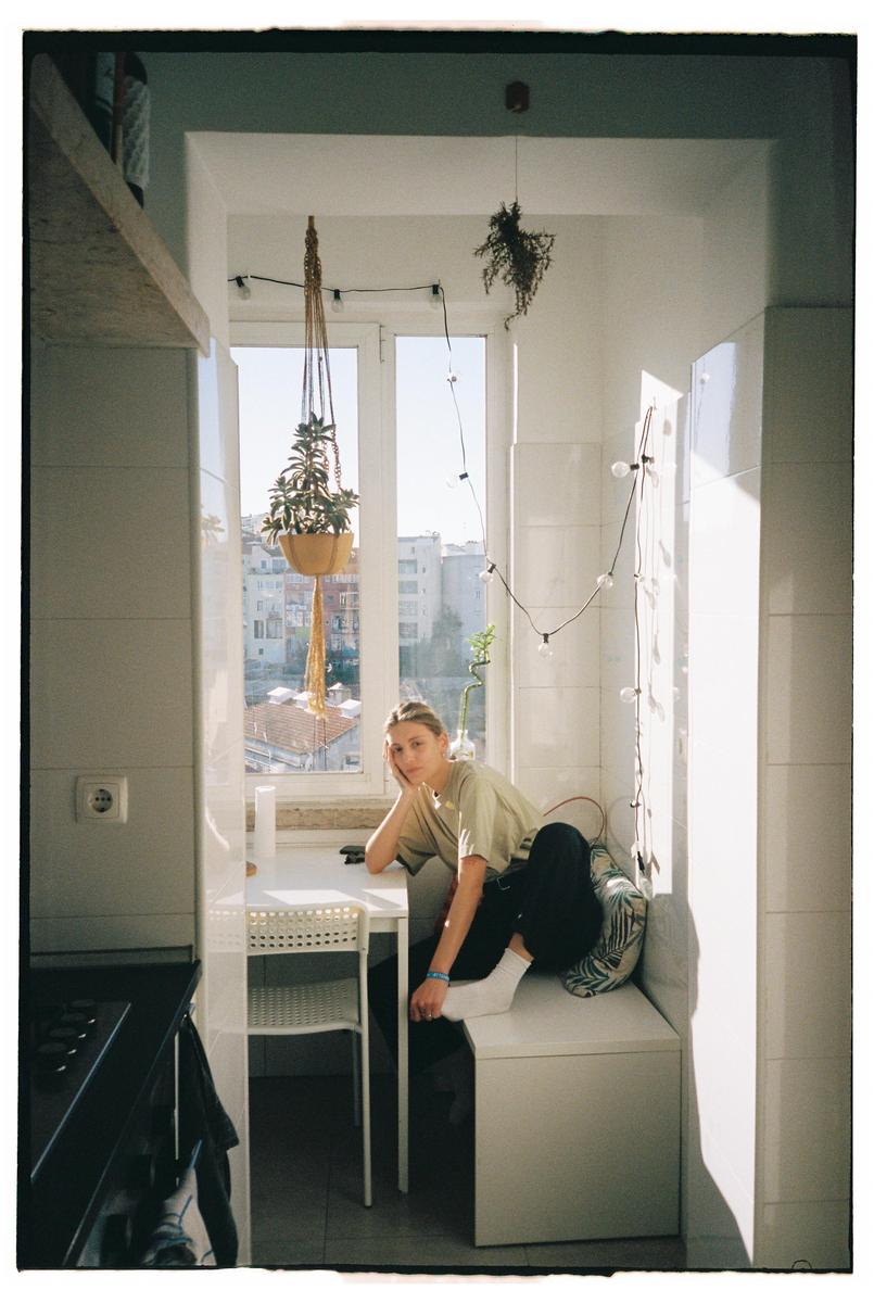 A woman sits at a table in a sunlit kitchen with a view of a city.