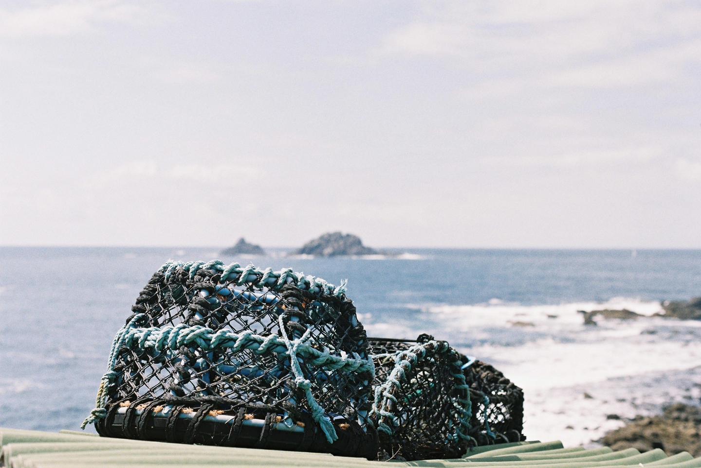Two lobster pots sit on a corrugated roof with the ocean and rocky islets in the background.