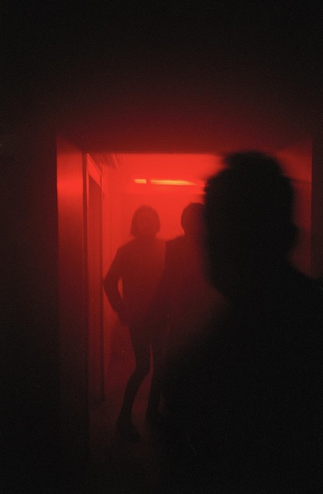 Three people are visible in a dark room illuminated by red light.