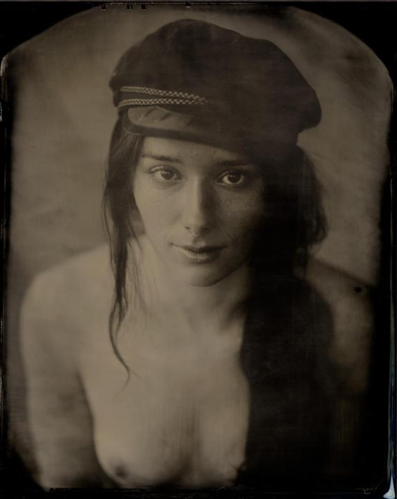 A woman with long hair and a hat looks directly at the viewer.