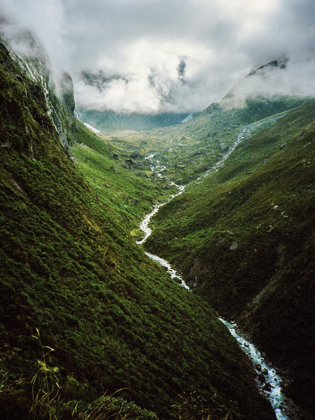 A river flows through a valley surrounded by mountains under a cloudy sky.