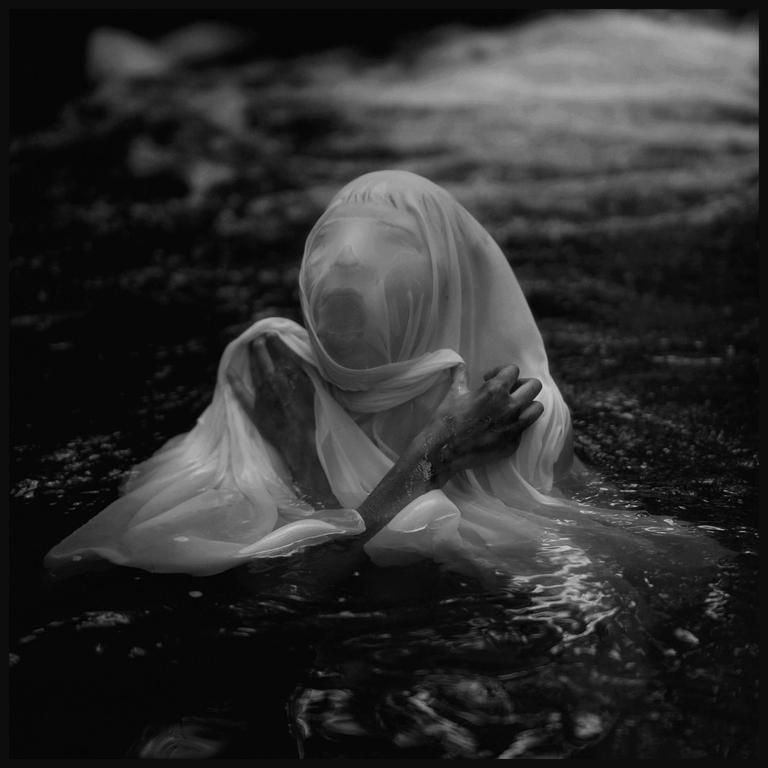 A person with a translucent cloth over their head and body is partially submerged in water.