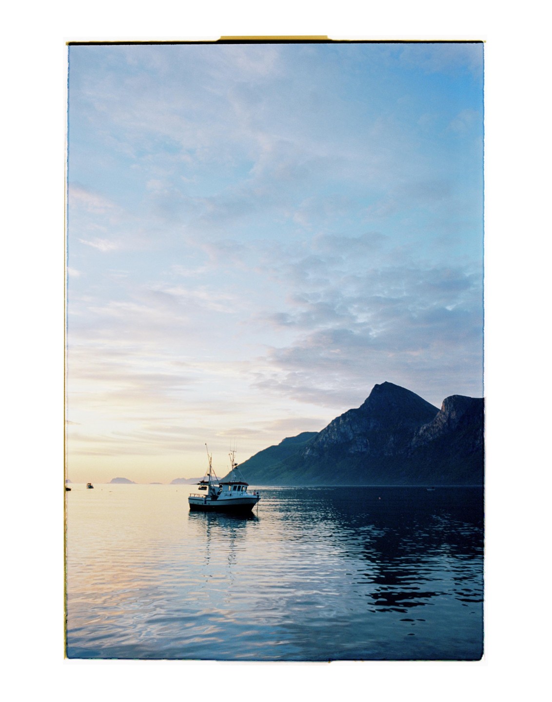 A boat floats on calm water with mountains in the background under a cloudy sky.