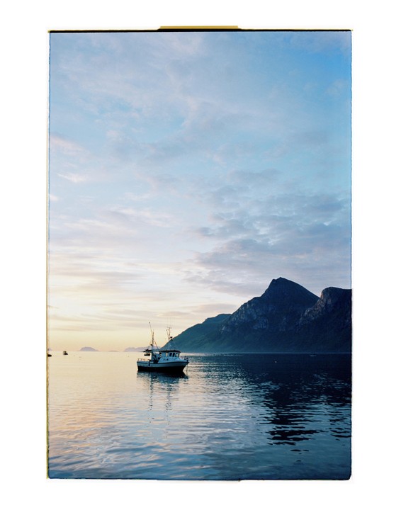 A boat floats on calm water with mountains in the background under a cloudy sky.