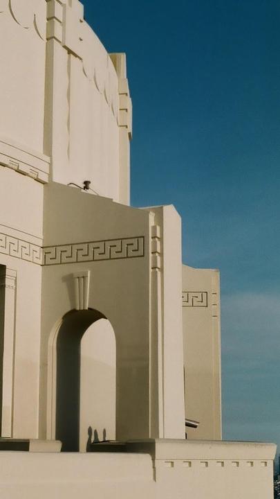 A white building with geometric patterns and arched doorways stands against a clear blue sky.