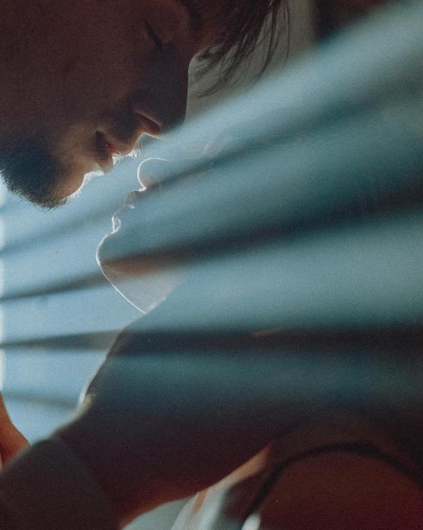 A man and woman are about to kiss, with light streaming through blinds onto their faces.