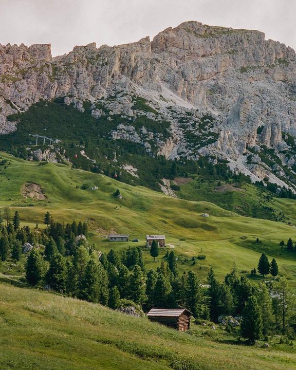 A mountain landscape shows a green valley with several small wooden cabins and a rocky mountain in the background.