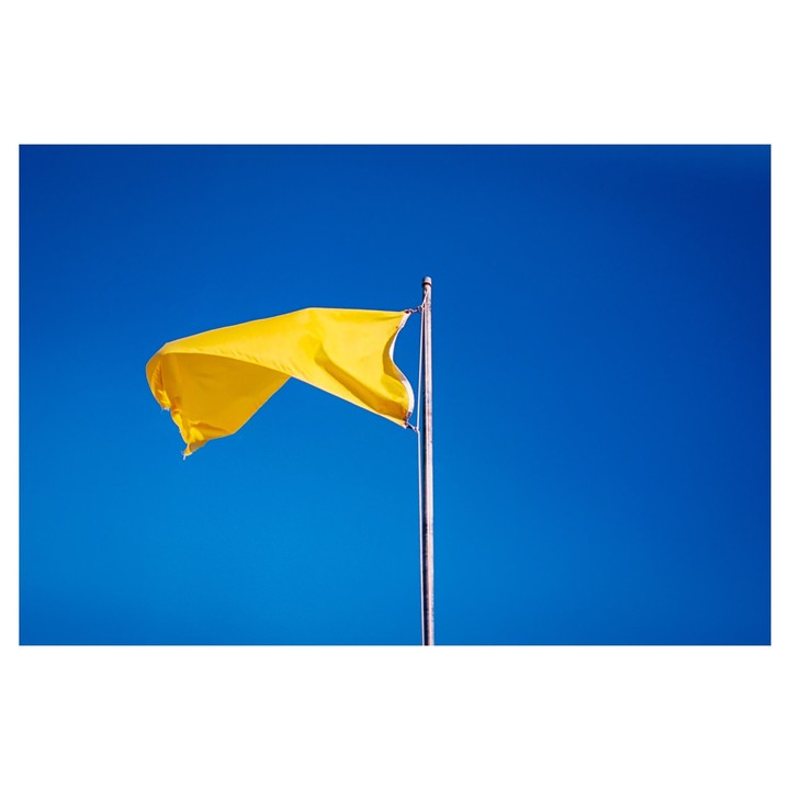 A bright yellow flag waves against a clear blue sky.