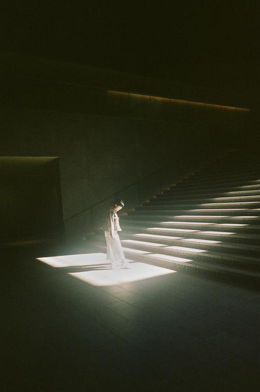 A woman stands in a spotlight at the bottom of a long staircase.