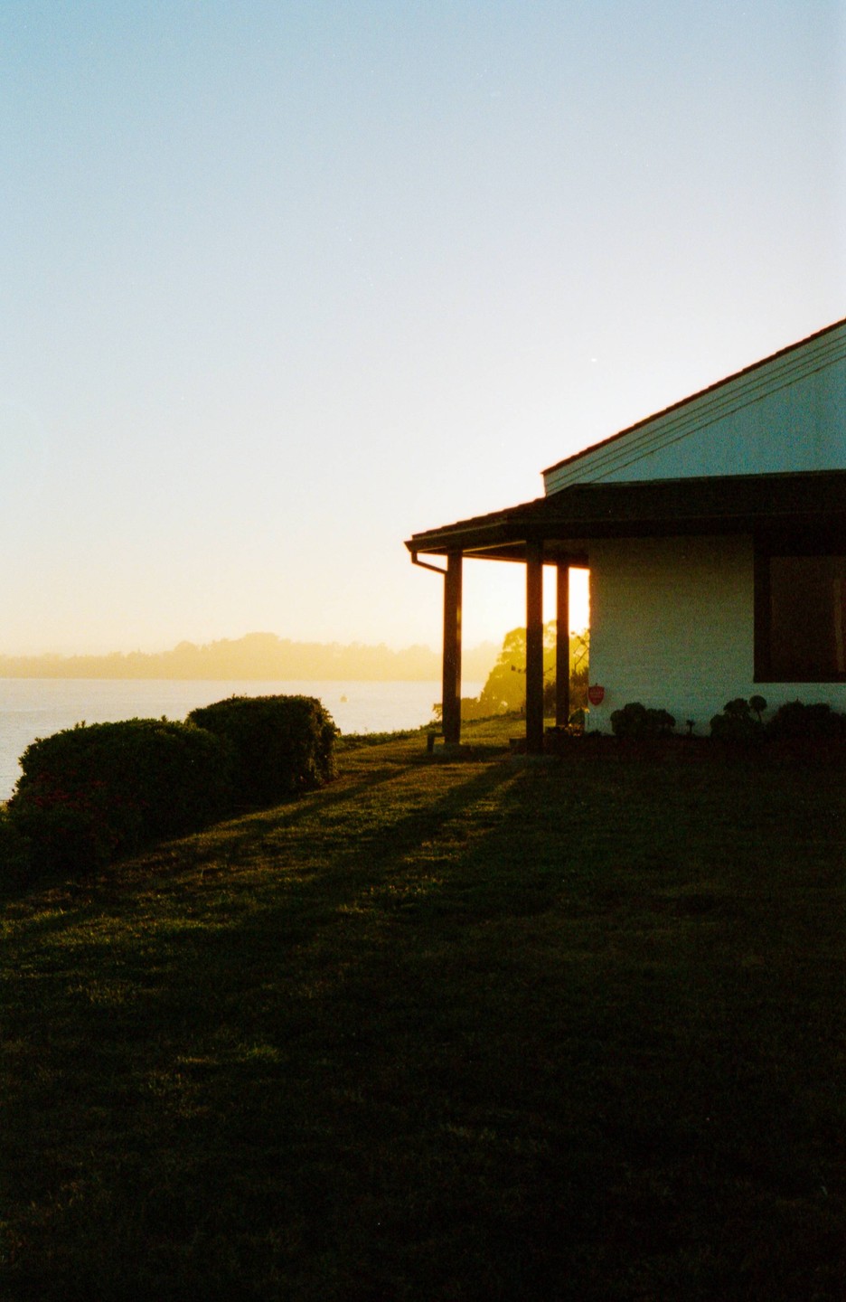 A house with a porch overlooks a body of water at sunset.